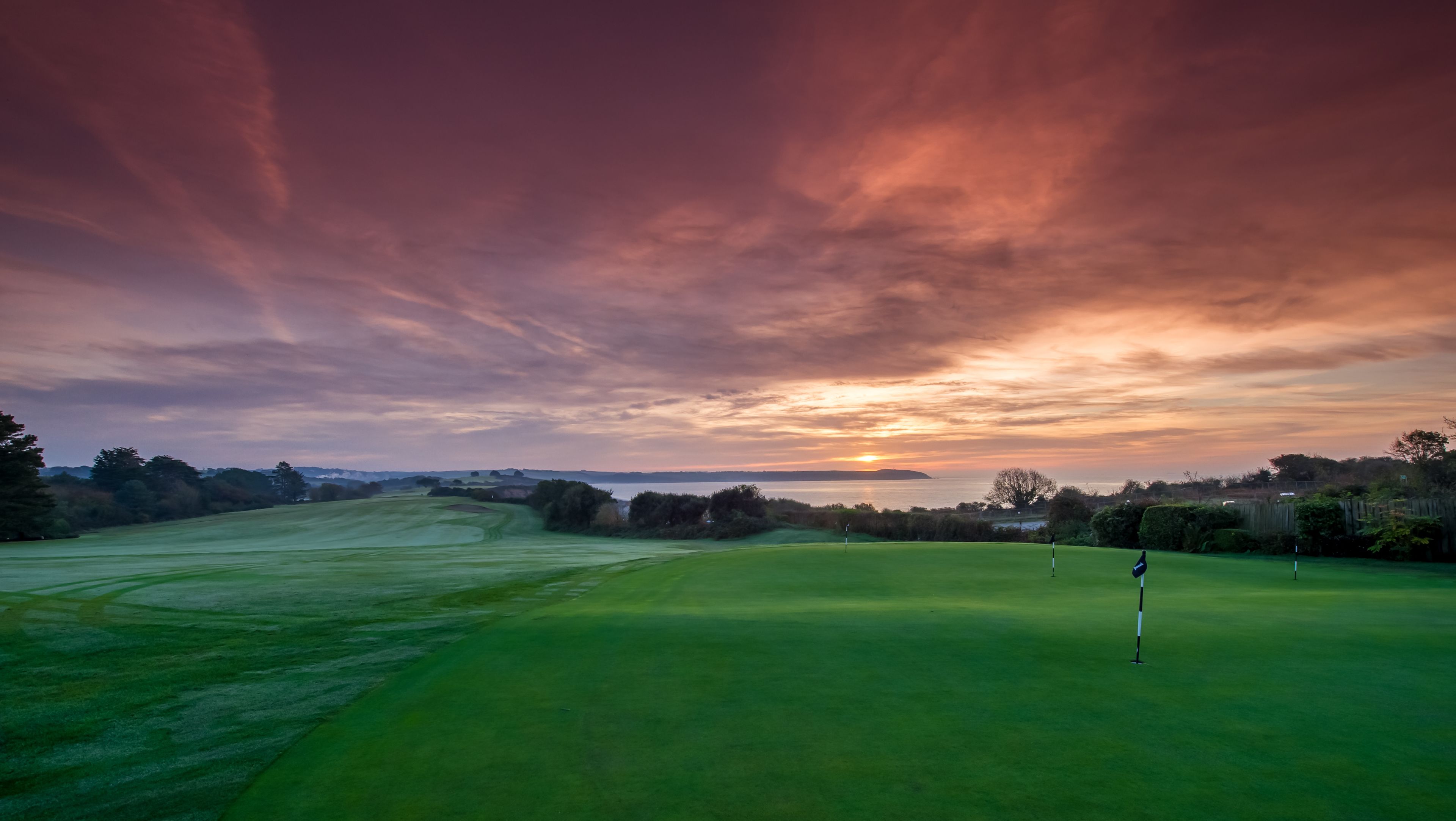 A golf course with a flagstick in the foreground and a sunset in the background.