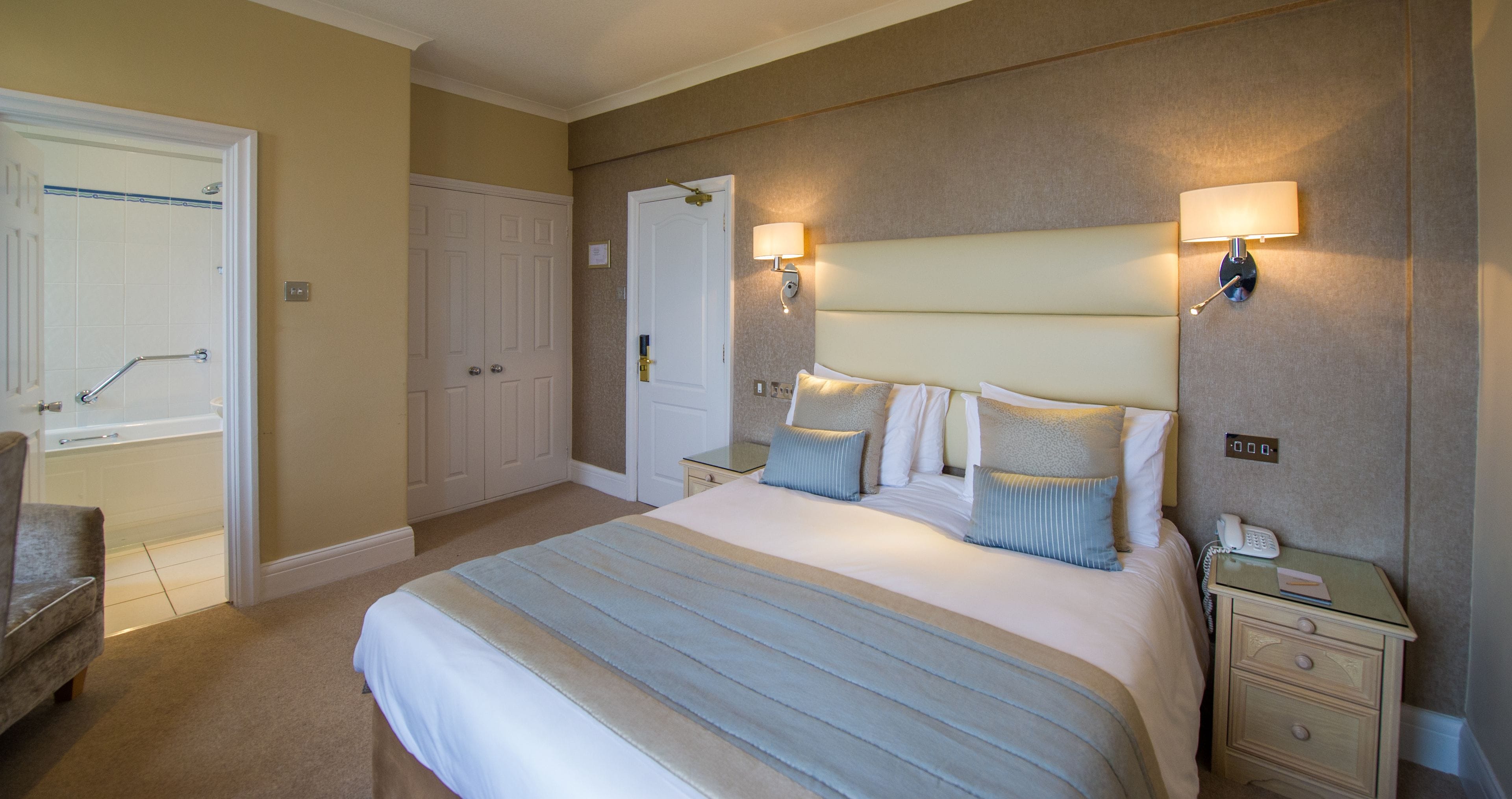 A hotel room with a large bed, bedside lamps, a nightstand, a chair, and a door leading to a bathroom.