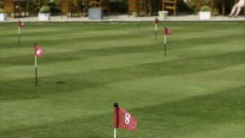 A golf course with a flag marked '8' on the green, surrounded by white umbrellas and a building with ivy-covered walls in the background.