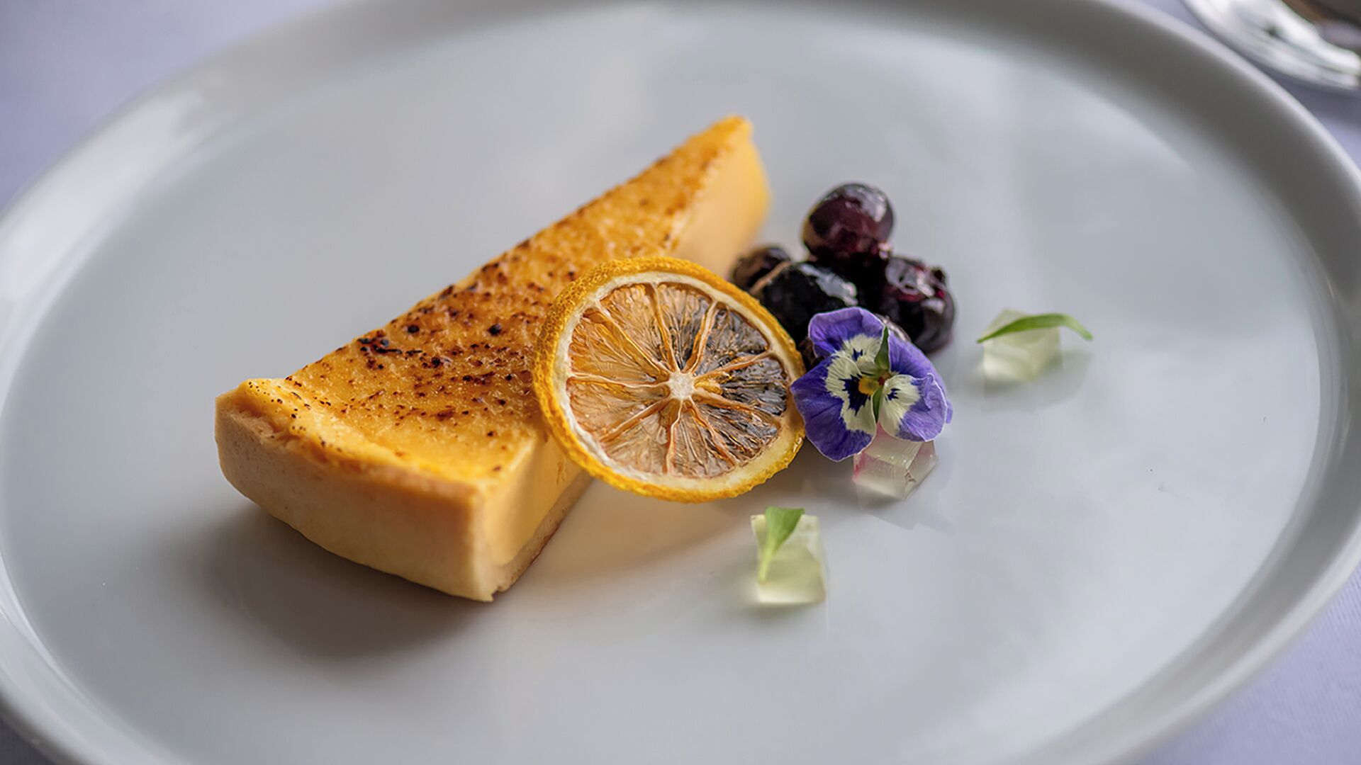 A dessert plate with a piece of cake, a dried orange slice, and a flower.