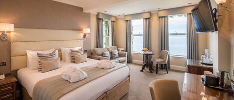 A hotel room with a large bed, a desk, a chair, a TV, and a view of the sea.