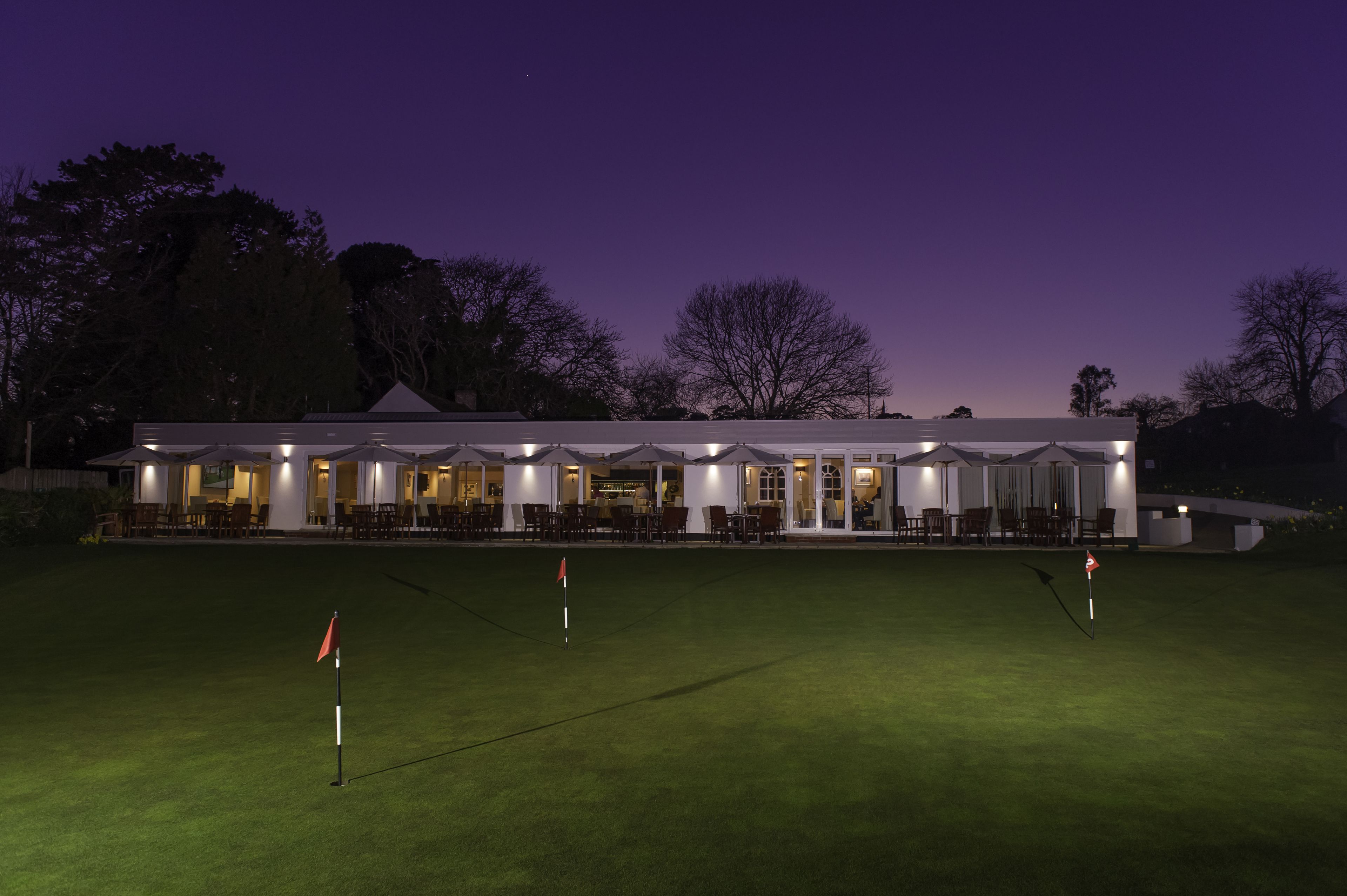 Un campo de golf al anochecer con un club de campo al fondo.