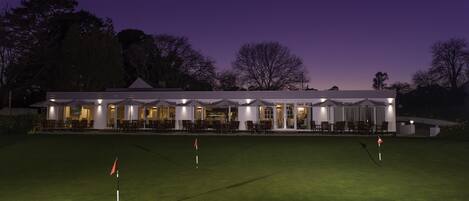 Un campo de golf al anochecer con un club de campo al fondo.