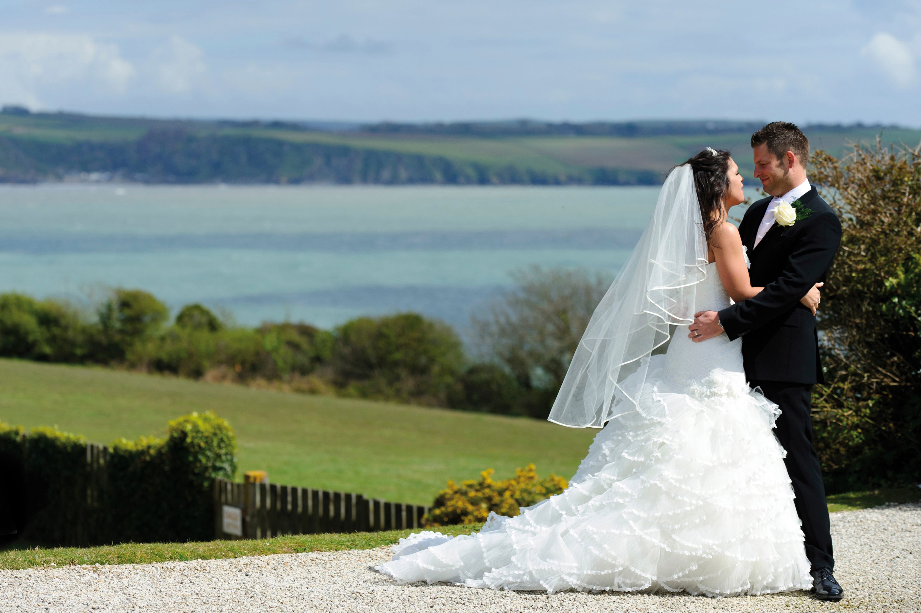 Una pareja abrazándose, la novia con vestido de novia y el novio con traje, con una vista panorámica al fondo.