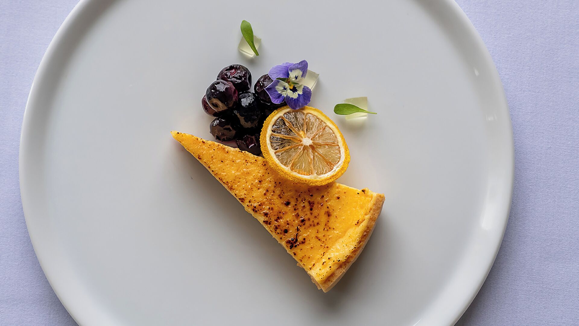 A white plate with a grilled cheese sandwich, a slice of lemon, and some grapes and flowers.