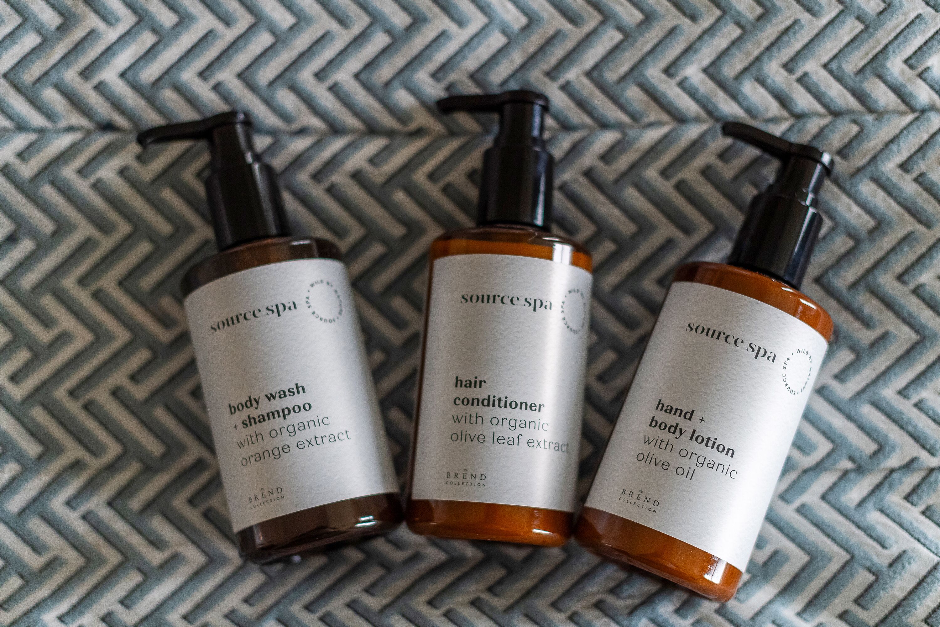 Three bottles of Source Spa body wash, hair conditioner, and hand + body lotion with organic olive leaf extract.