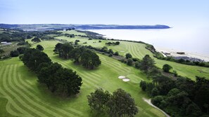 A golf course with bunkers, trees, and a beach in the background.