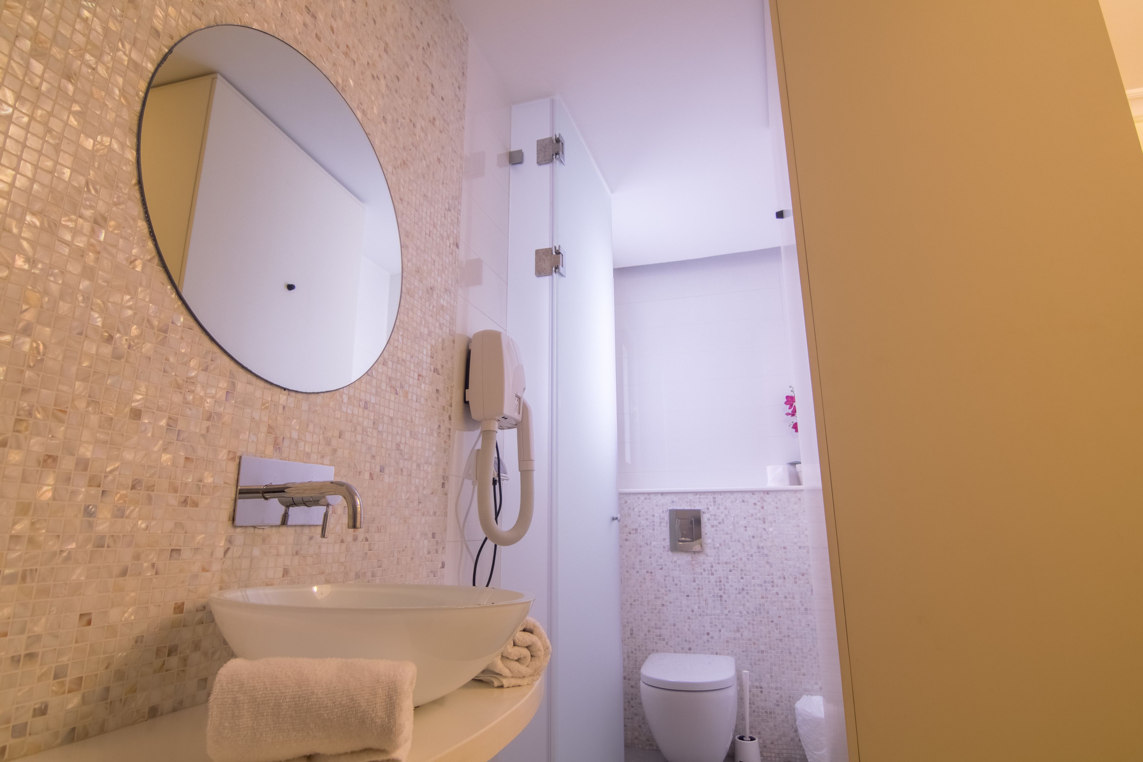 Un baño con lavamanos blanco, espejo, toalla, inodoro y ducha.