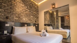A hotel room with a brick wall, a large bed, a bedside table with a phone and a menu, and a mirror reflecting the room. - The Bell Boutique Hotel (Tel Aviv)