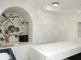 Un baño con lavamanos de mármol, un mural con motivos de árboles y una pared de piedra.