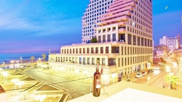 A modern hotel with a prominent glass facade, a rooftop terrace, and a view of the surrounding cityscape. - The Bell Boutique Hotel (Tel Aviv)