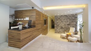 A reception area with a wooden reception desk, a stone wall, and a seating area with chairs and a small table. - The Bell Boutique Hotel (Tel Aviv)