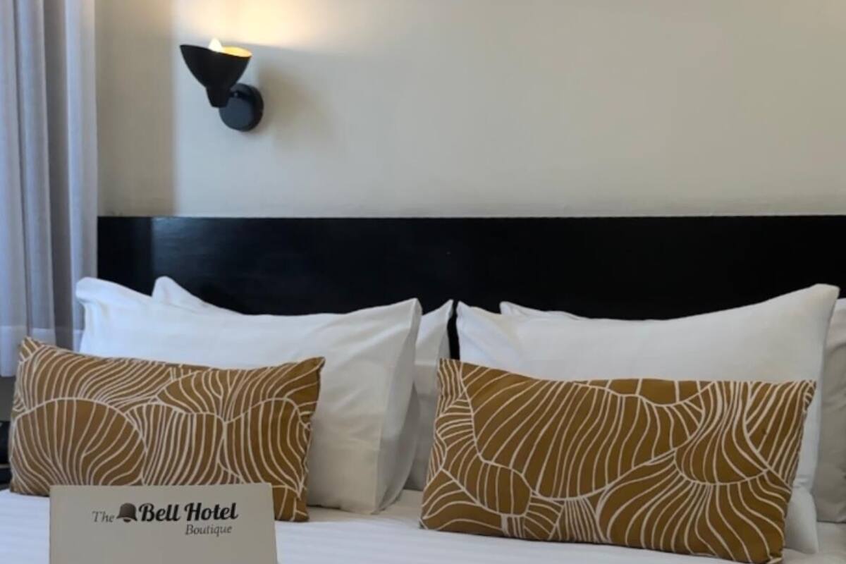 A hotel room with a neatly made bed, a sign for The Bell Boutique, and a wall-mounted light fixture.