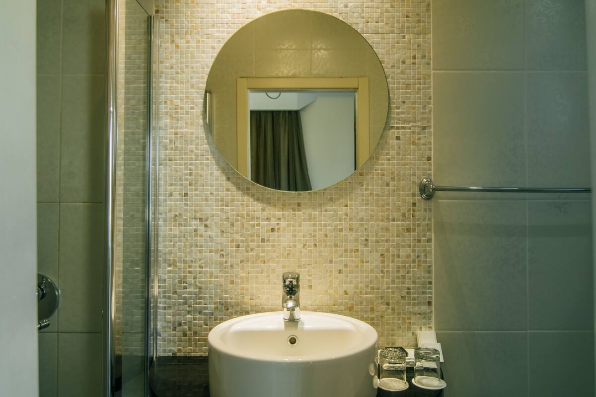 A bathroom with a round mirror, a sink, and a tiled wall.