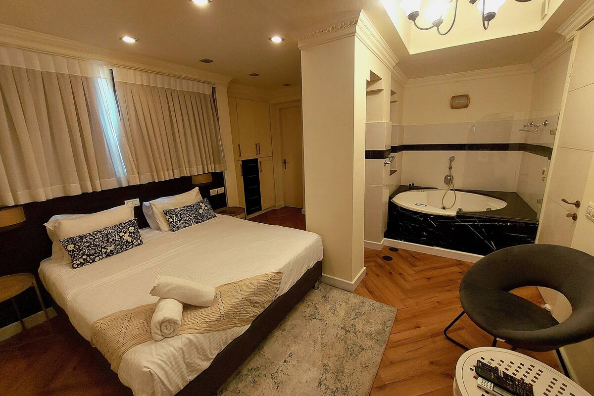 A hotel room with a bed, a bathroom with a bathtub, and a chair.