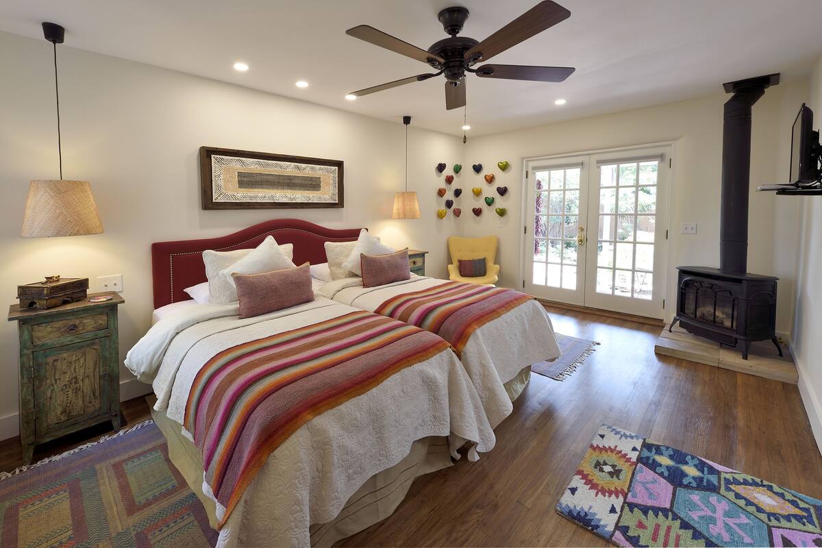 A bedroom with two beds, a ceiling fan, a fireplace, and a large window.