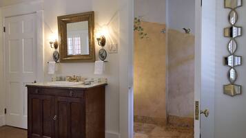 A bathroom with a wooden vanity, a mirror with wall sconces, and a shower area.