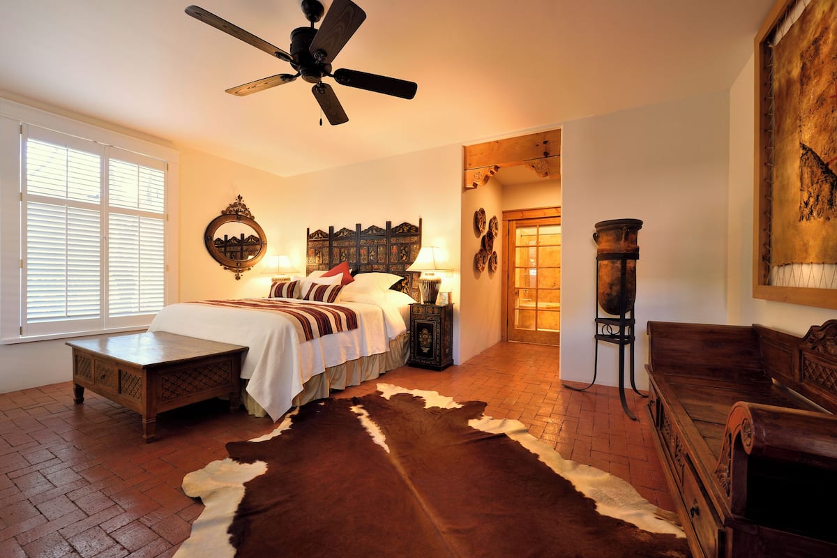 A bedroom with a bed, a wooden bench, a cowhide rug, a ceiling fan, and a rustic wall decor.