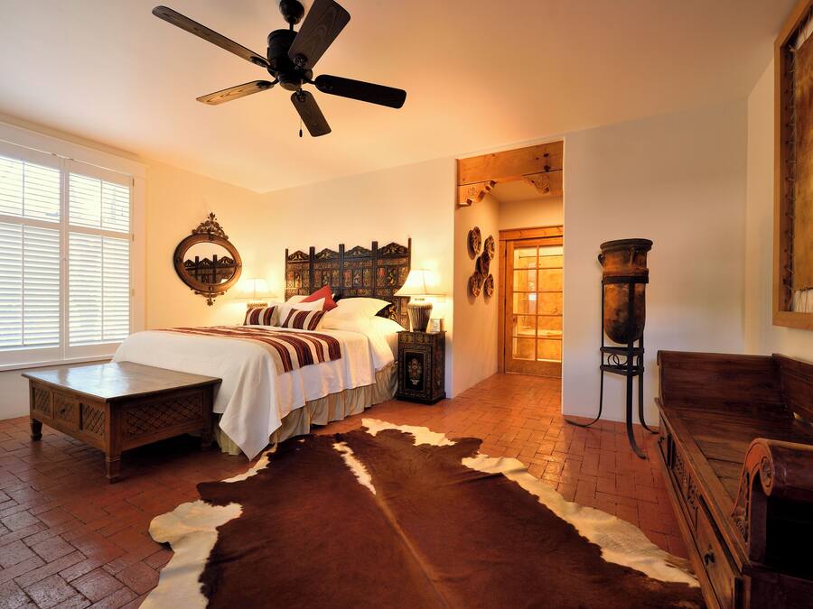 Ein Schlafzimmer mit einem Bett, einer Holzbank, einem Kuhfellteppich, einem Deckenventilator und rustikaler Wandgestaltung.