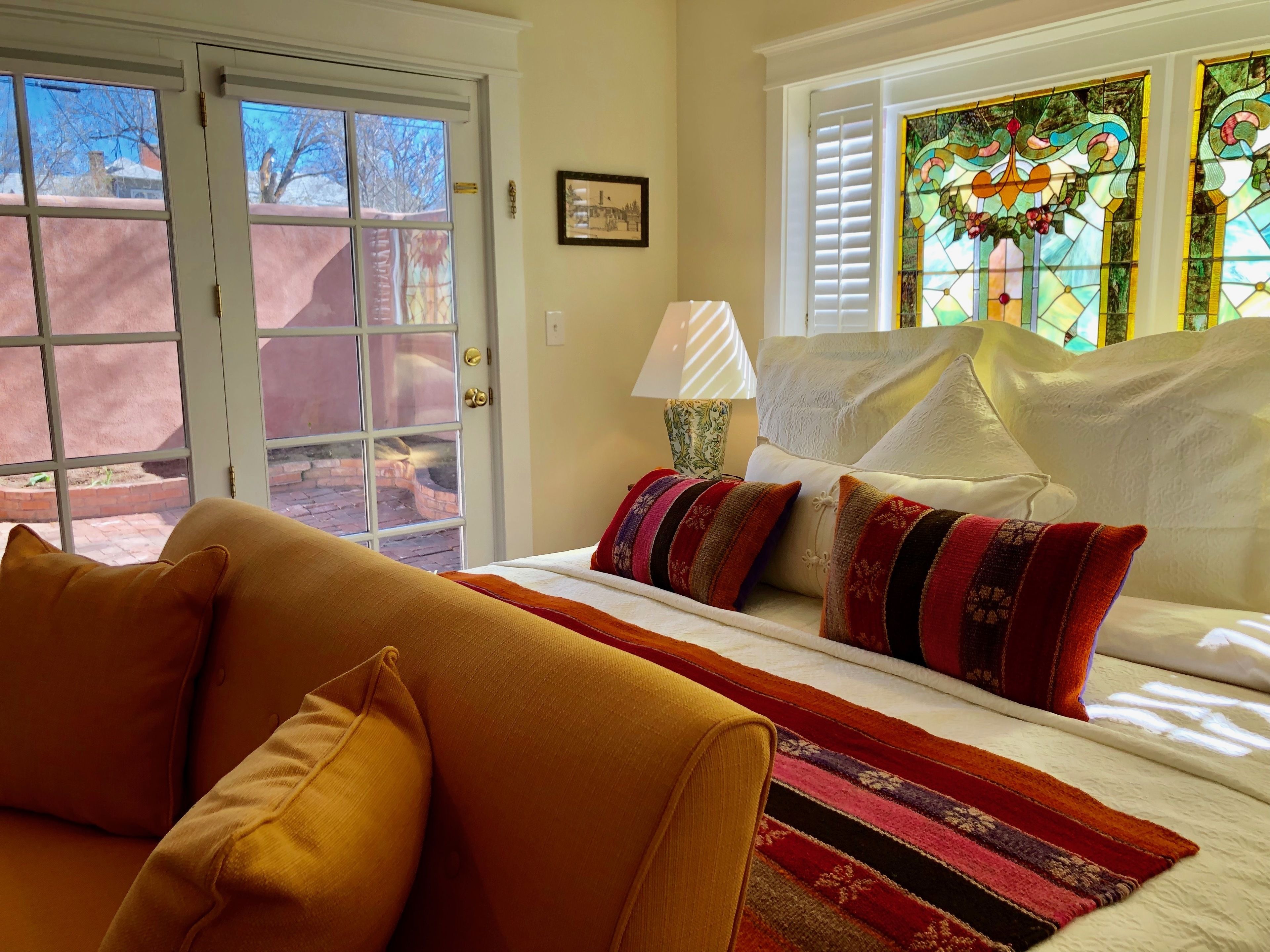 Quarto com cama, sofá, luminária e janela com design em vitral.