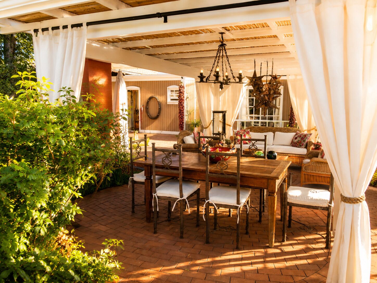 A covered patio with a wooden table and chairs, a hanging star chandelier, and a wicker sofa.