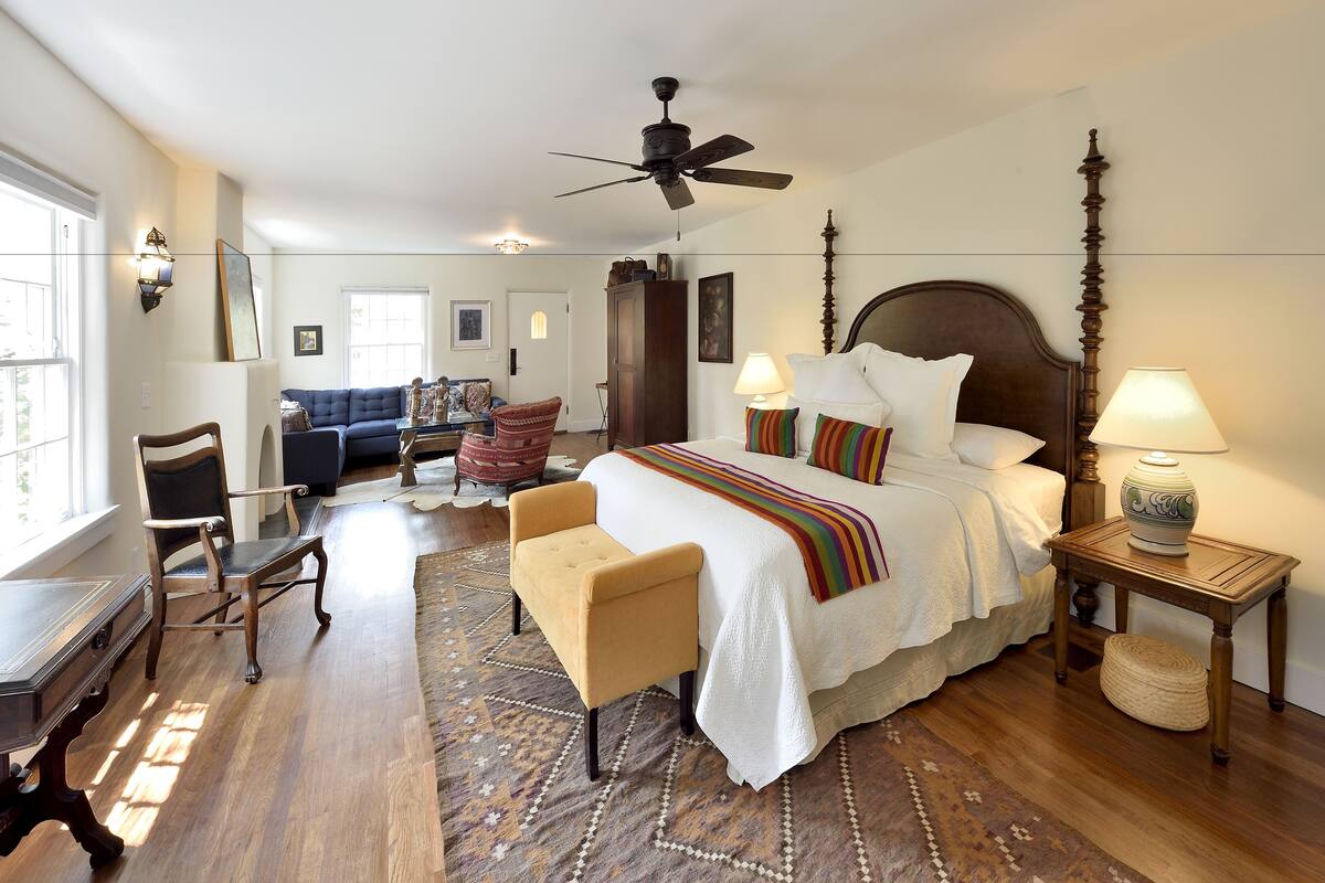 A bedroom with a large bed, a ceiling fan, a wooden nightstand, and a patterned rug.