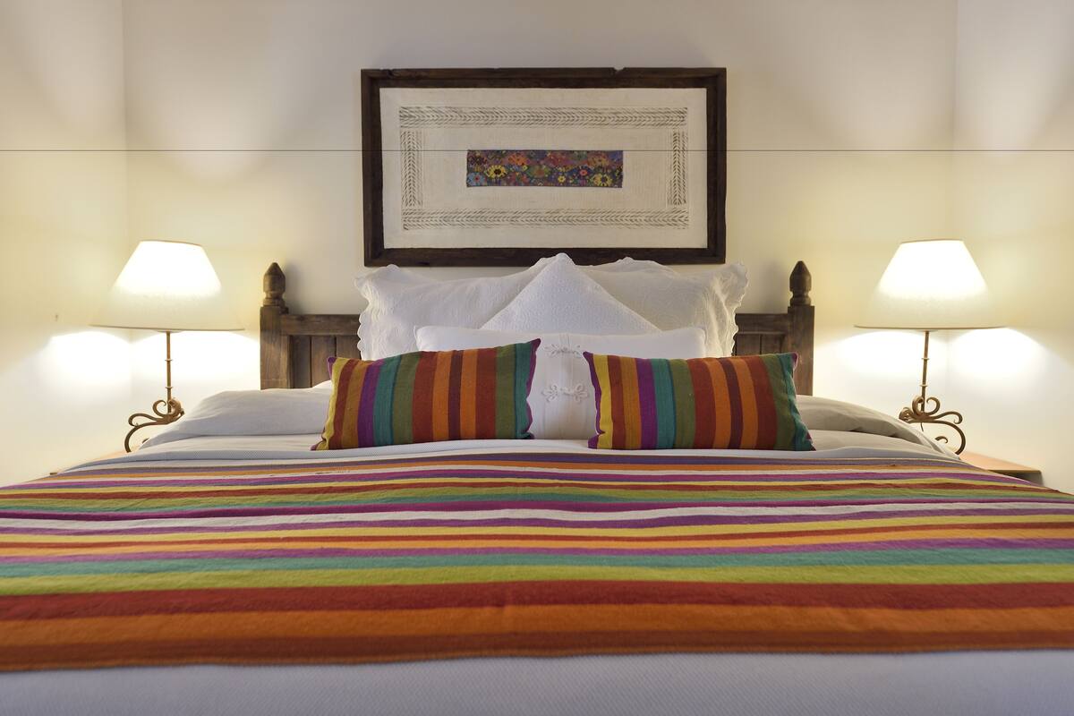 A neatly made bed with a colorful striped blanket, two pillows, and a framed artwork above it.