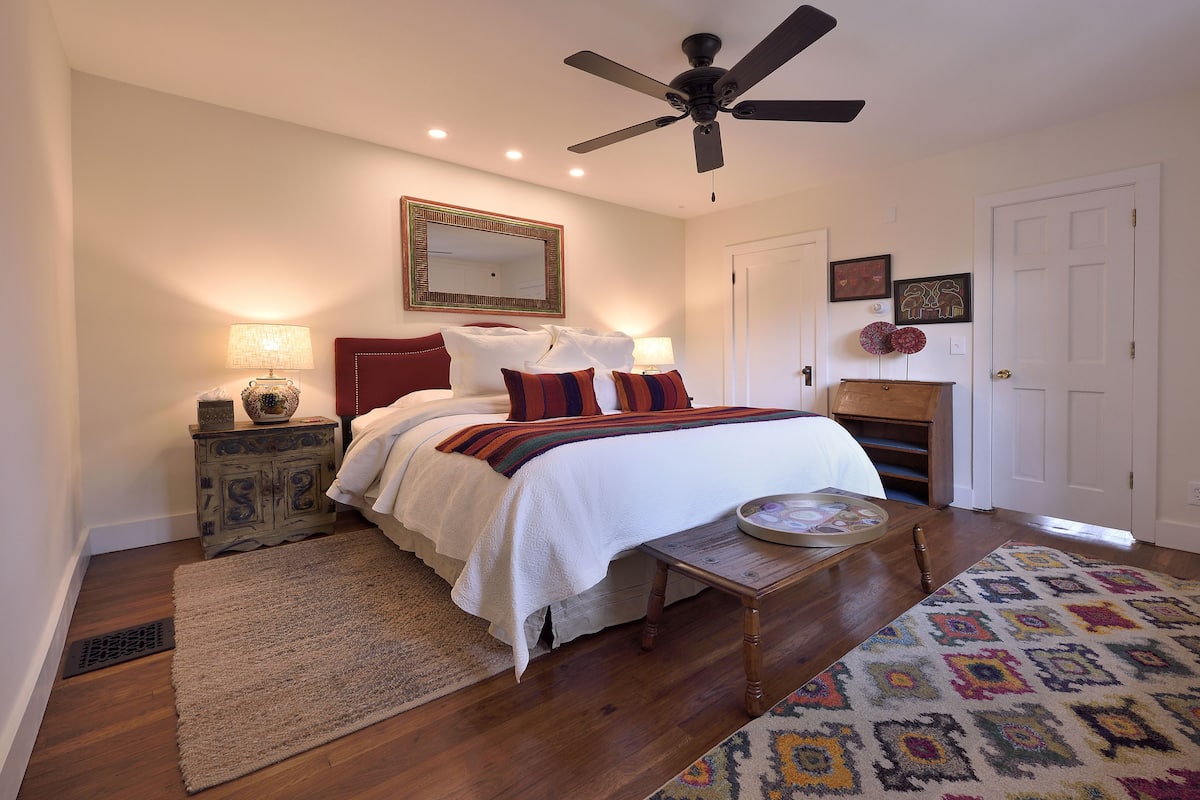 A bedroom with a bed, a ceiling fan, a nightstand, a dresser, and a patterned rug.
