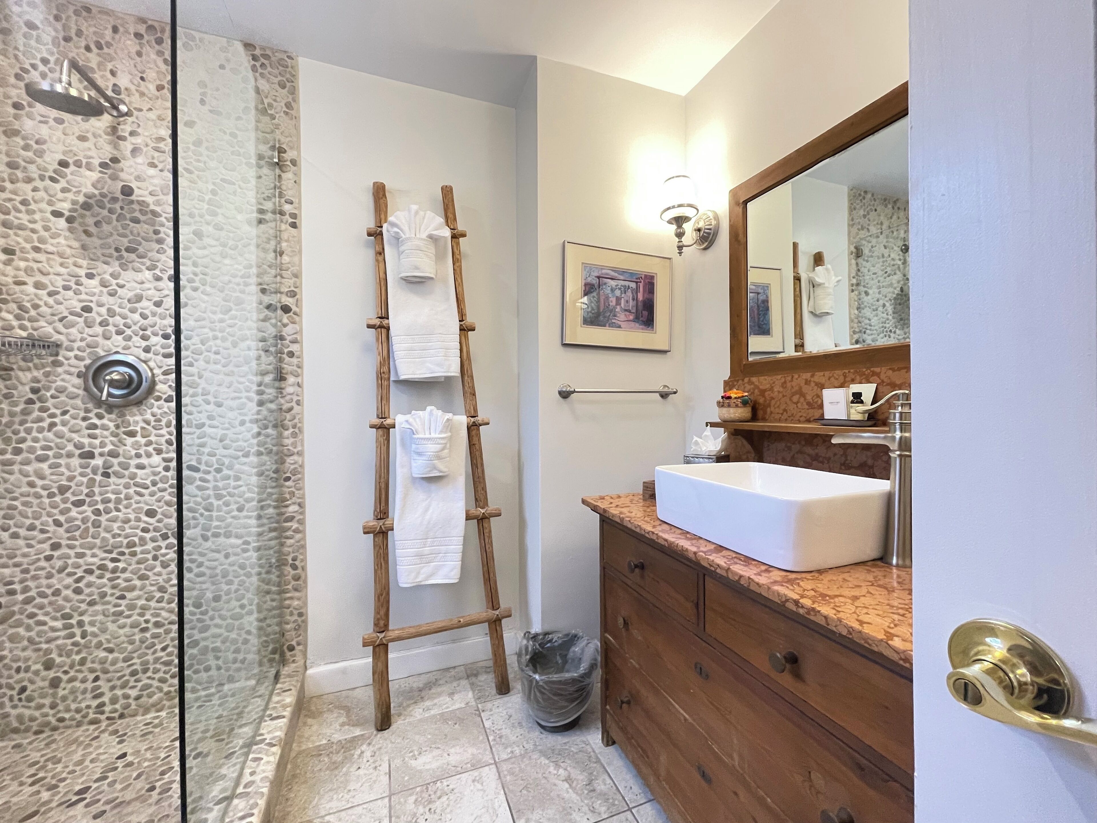 Un bagno con cabina doccia in pietra, porta asciugamani in legno, lavabo con piano in marmo e specchio sopra il lavabo.