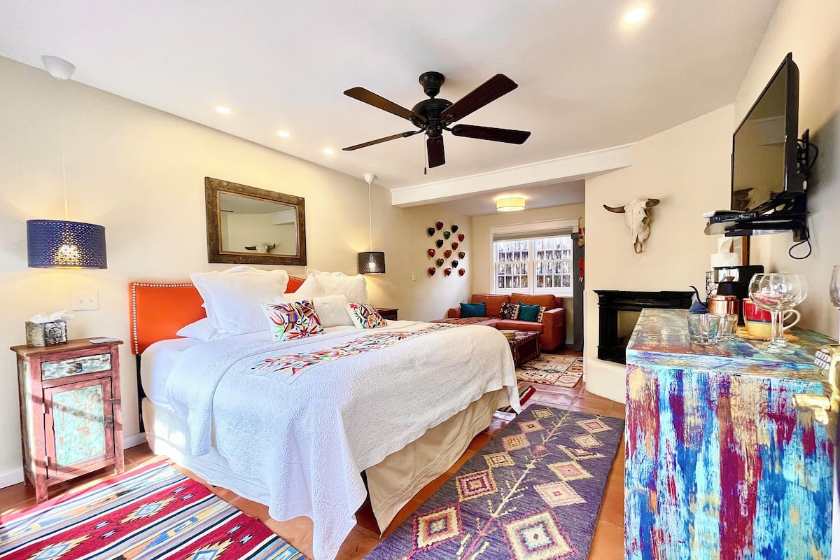 A bedroom with a bed, a ceiling fan, a fireplace, and a coffee table.