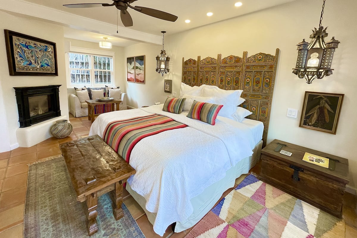 A bedroom with a large bed, a ceiling fan, a fireplace, and a wooden headboard.
