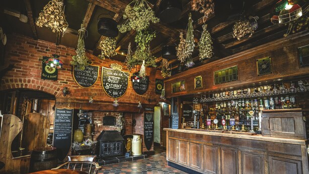 A rustic bar with wooden furnishings, a brick wall, and hanging plants. - Hundred House Hotel (Shifnal)