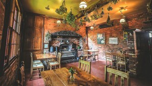A rustic interior with exposed brick walls, a brick fireplace, hanging plants, and wooden furniture. - Hundred House Hotel (Shifnal)