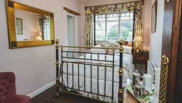 A bedroom with a four-poster bed, a large mirror, floral curtains, and a view of greenery outside.