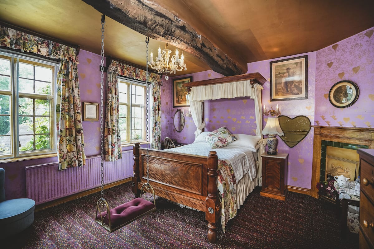 A bedroom with a wooden four-poster bed, a hanging chair, and a fireplace.