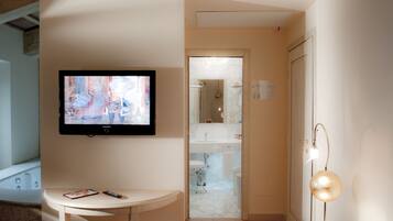 Un baño moderno con una televisión montada en la pared, una mesita con un control remoto y un teléfono, y una lámpara de pie.