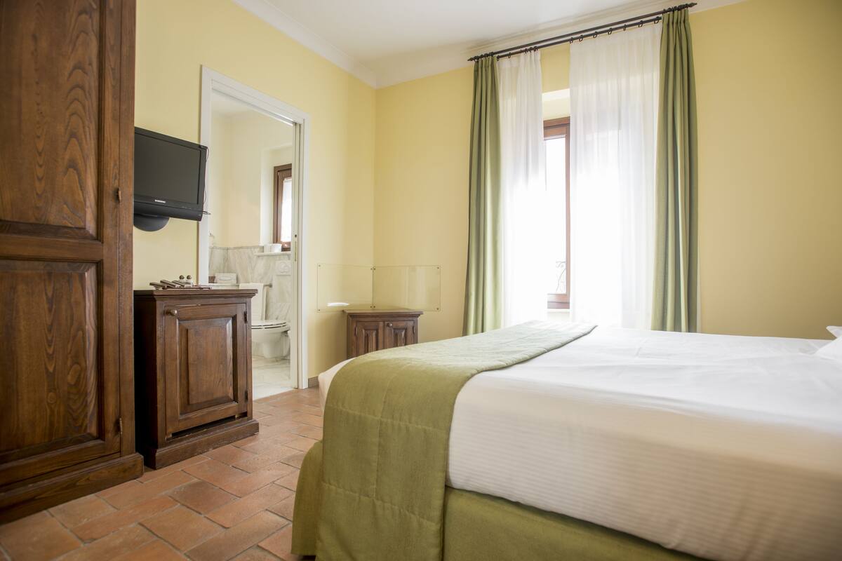 A hotel room with a bed, wooden wardrobe, a television, and a bathroom visible through an open door.