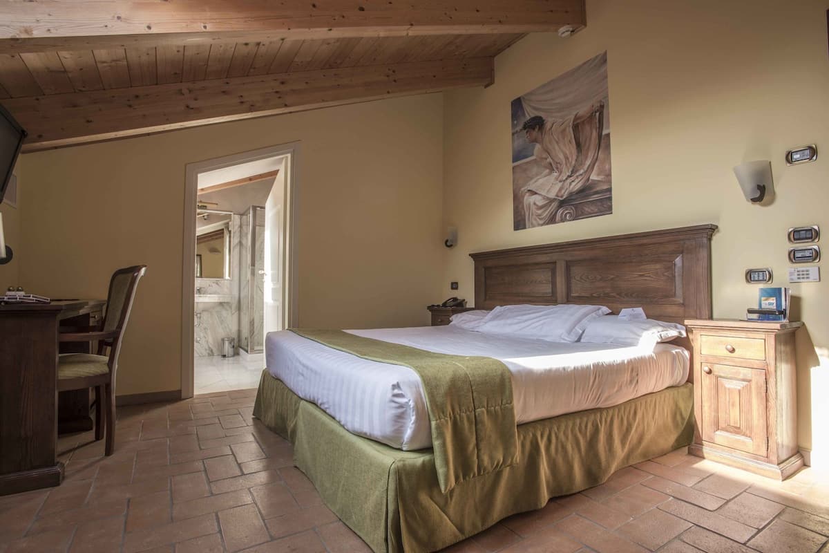 A bedroom with a bed, a desk, a chair, a wooden headboard, and a painting on the wall.