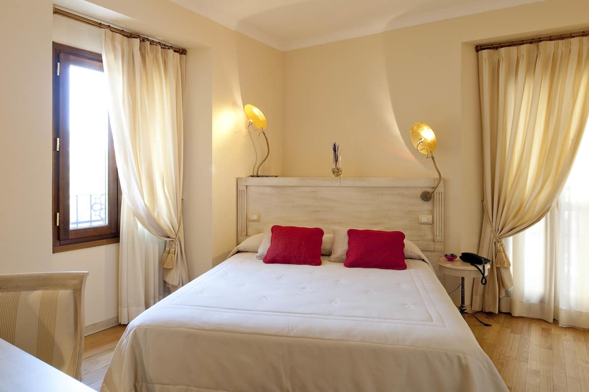 A hotel room with a large bed, two red pillows, a bedside table with a lamp, and a phone.