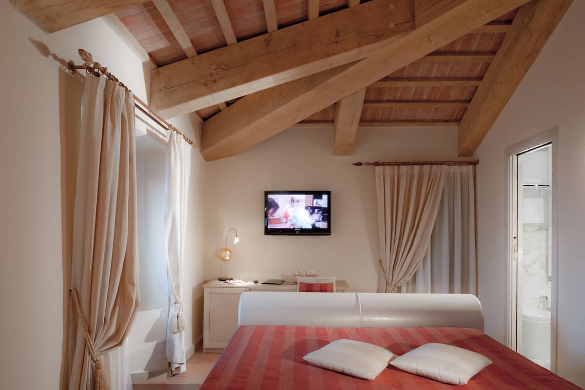 A bedroom with a wooden ceiling, a bed with a red and white striped bedspread, a television on the wall, and curtains on the windows.