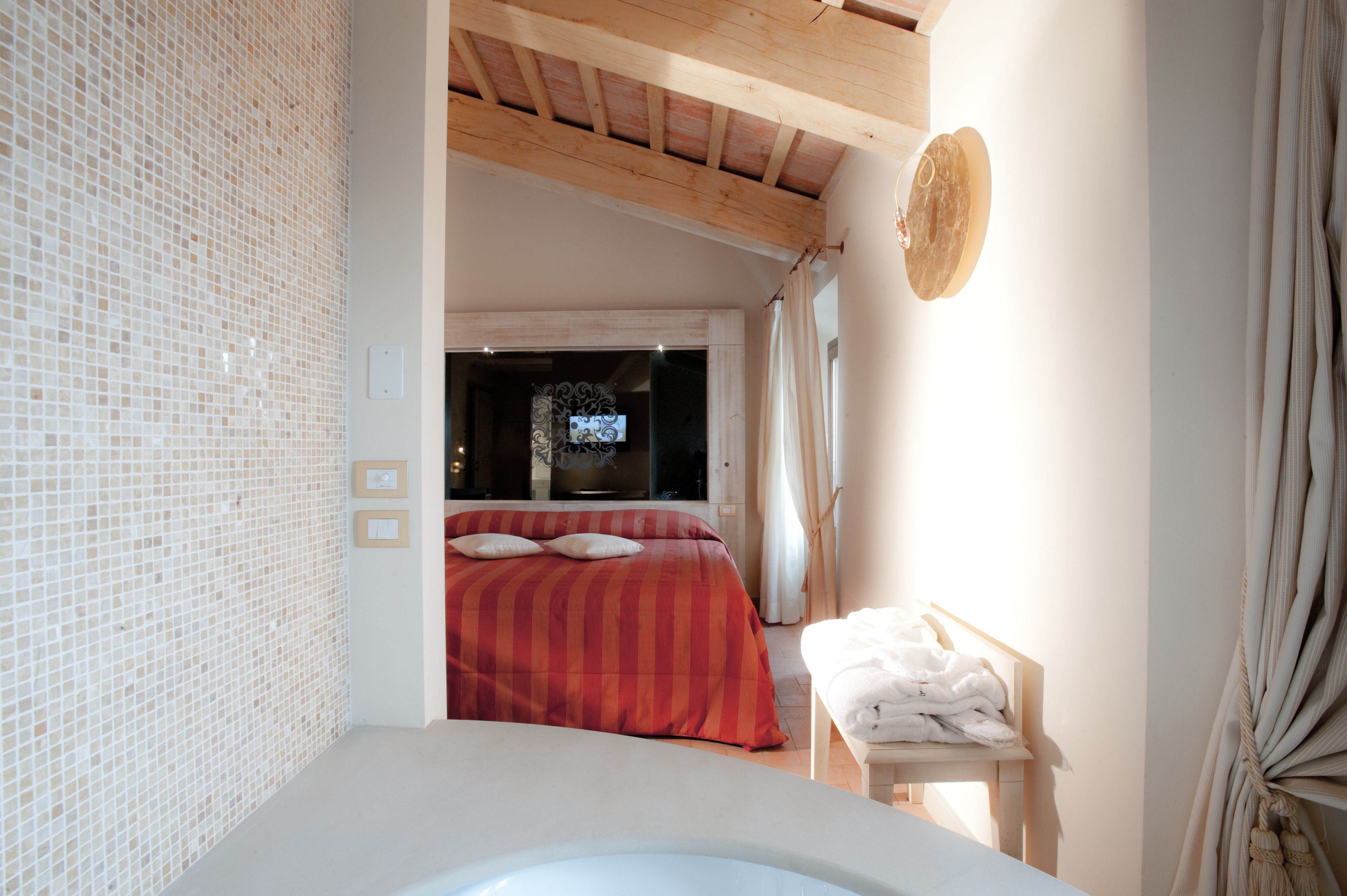A bedroom with a large bed, a small table with towels, and a view of the outside.