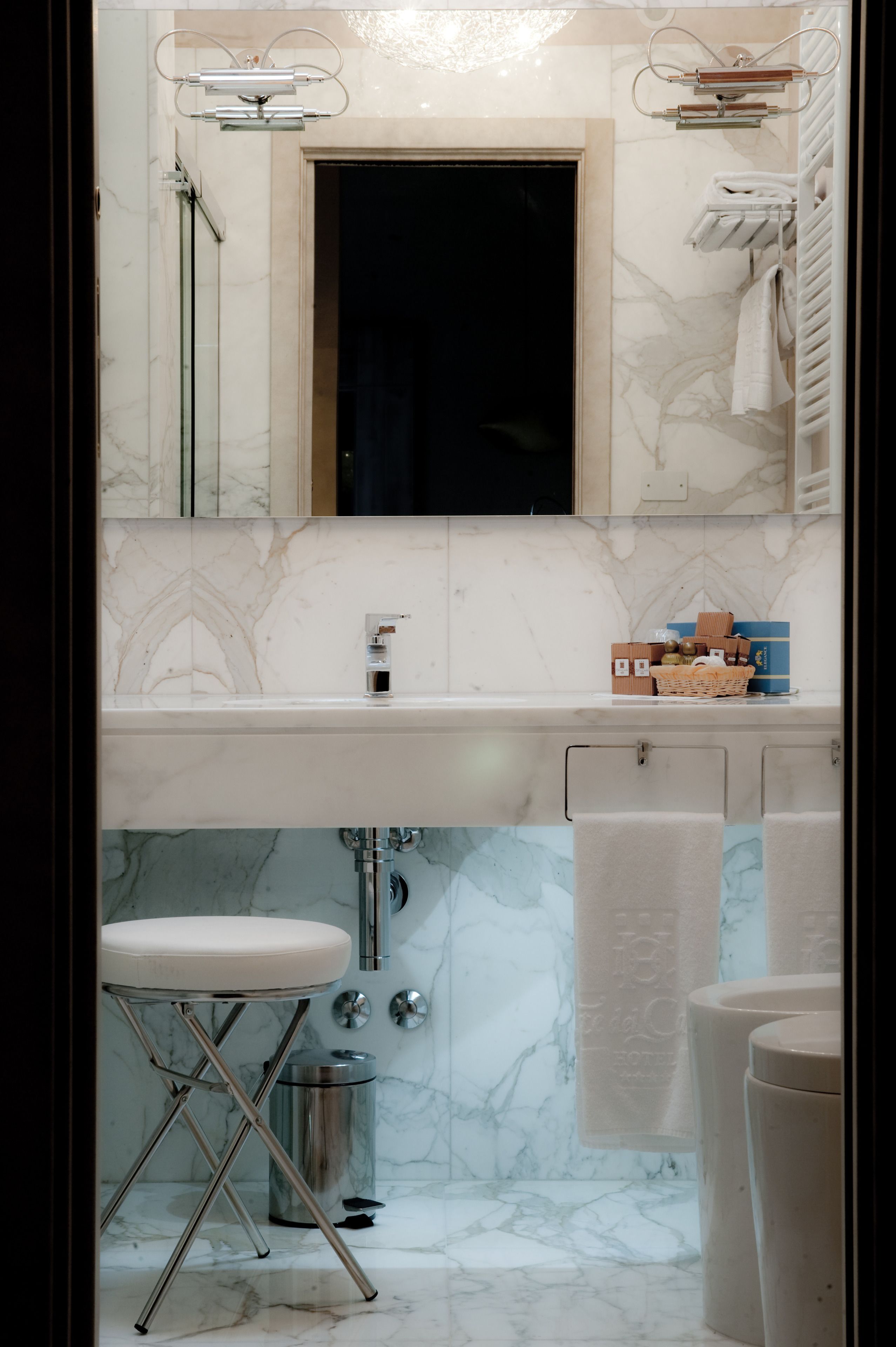 A bathroom with a marble sink, a mirror, a towel rack, and a small stool.