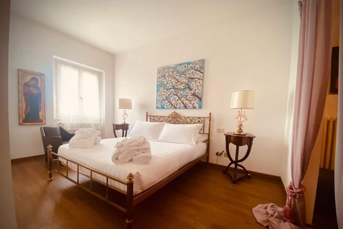A hotel room with a bed, two bedside tables, a chair, a window, and artwork on the walls.