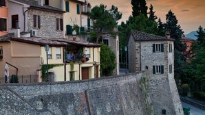 A historic stone wall with a stone tower and adjacent buildings with balconies and windows. - Oste del Castello Wellness & Bike Hotel (Verucchio)