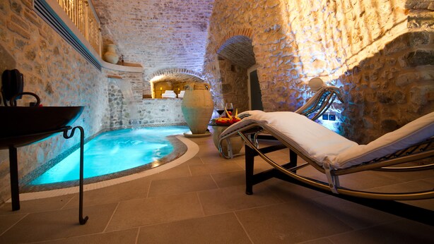 A spa area with a stone wall, a hot tub, and a lounge chair. - Oste del Castello Wellness & Bike Hotel (Verucchio)