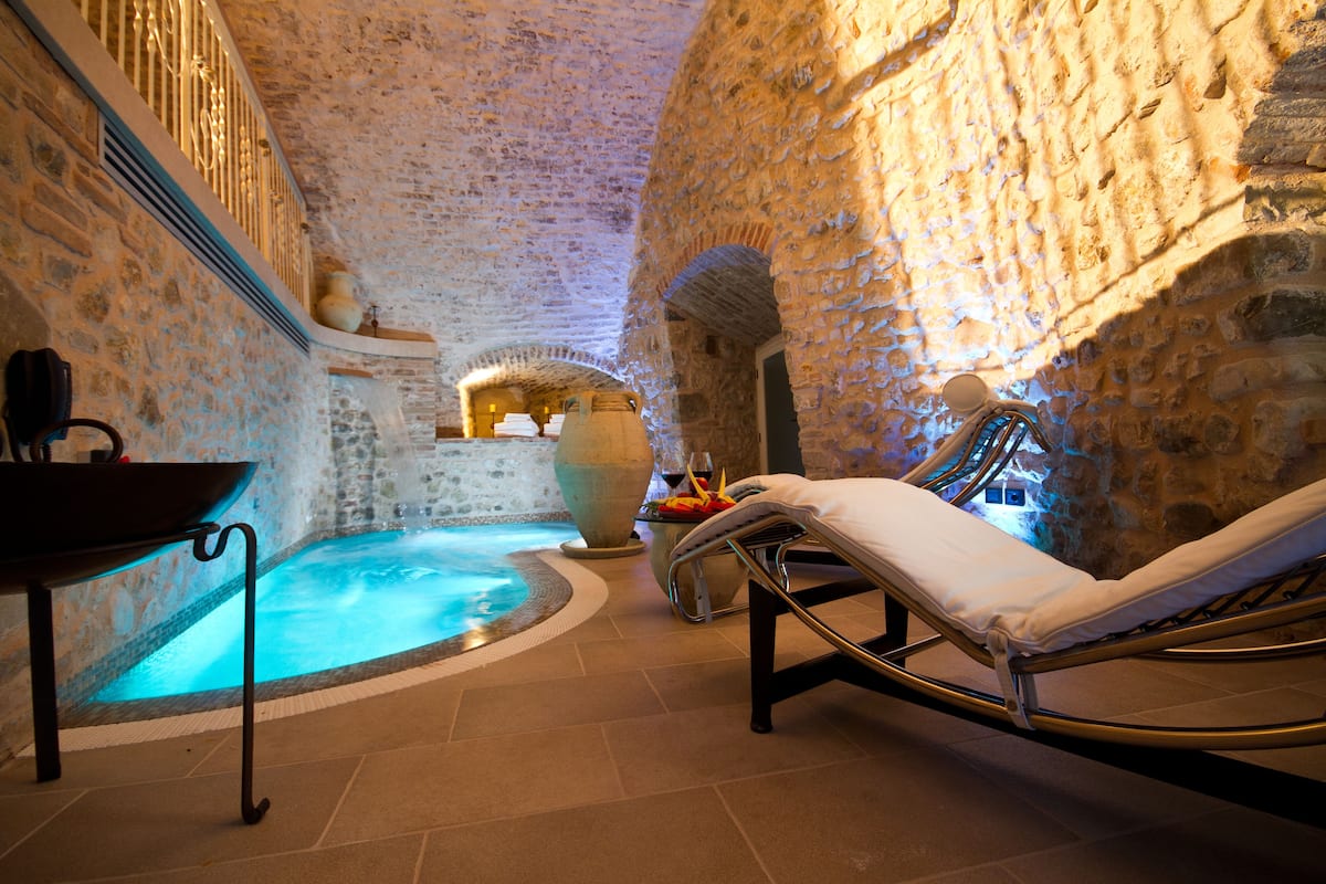 A spa area with a stone wall, a hot tub, and a lounge chair.