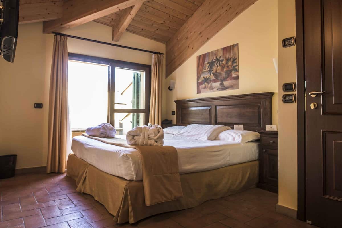 A hotel room with a wooden ceiling, a large bed with a headboard, a painting on the wall, and a door with a keypad lock.