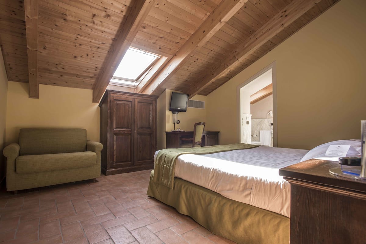 A bedroom with a wooden ceiling, a bed, a sofa, a desk, and a television.