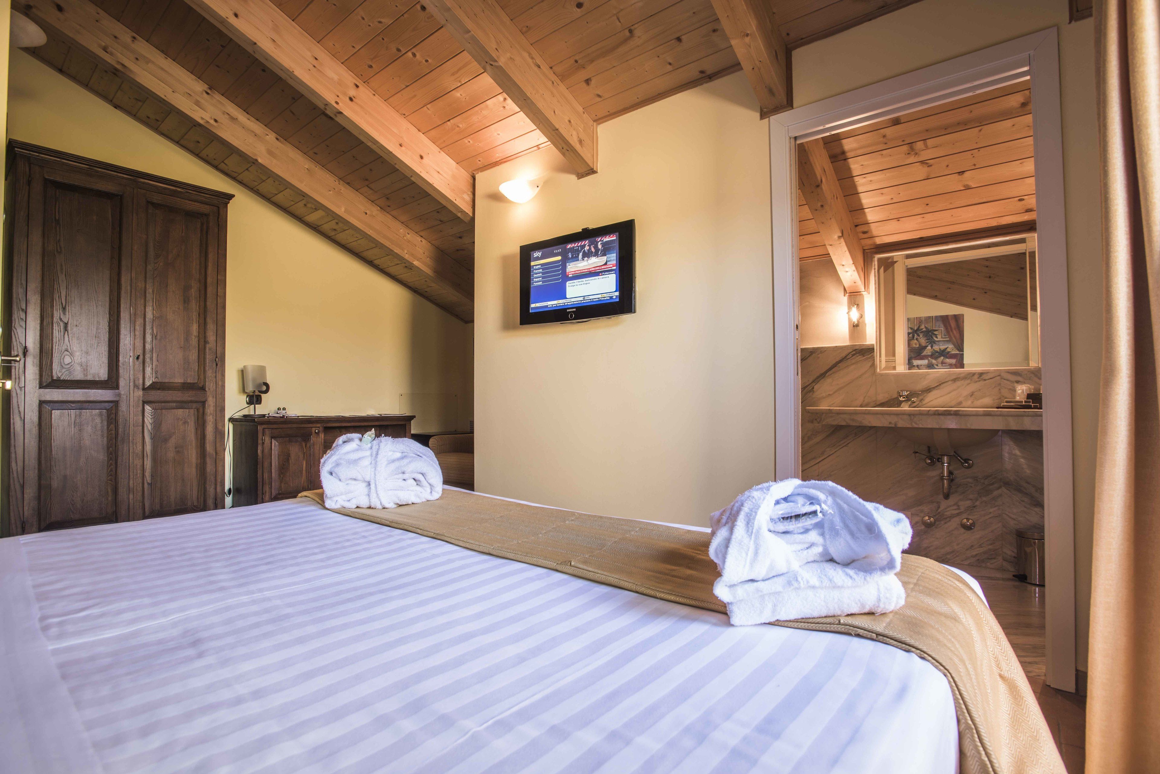 Habitació d'hotel amb un llit, bigues de sostre de fusta, una televisió i un bany visible a través d'una porta oberta.