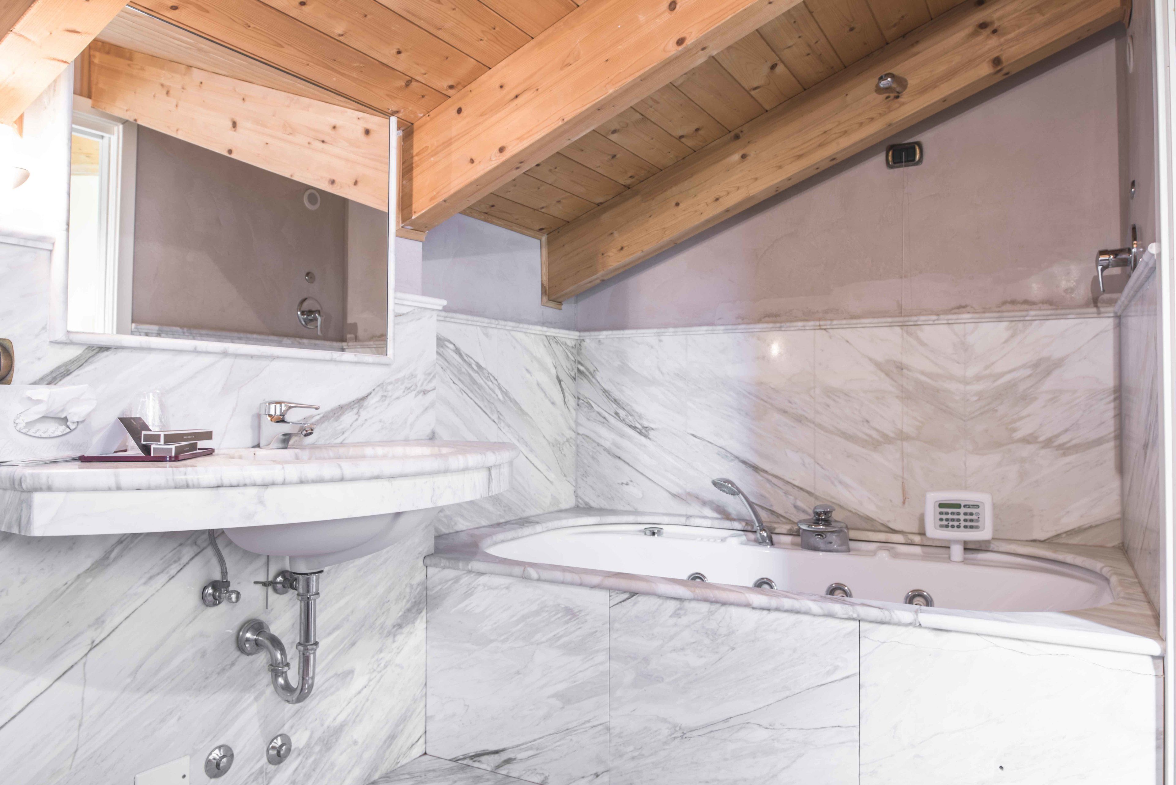 A bathroom with a marble sink, a bathtub, and a wooden ceiling.
